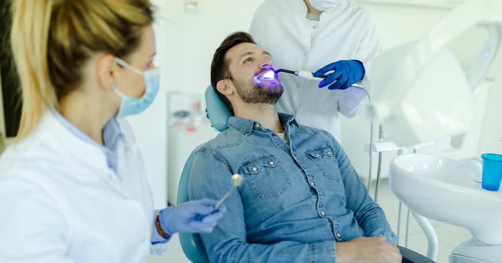 Photo of a male patient visiting dentist for teeth whitening in clinic.
